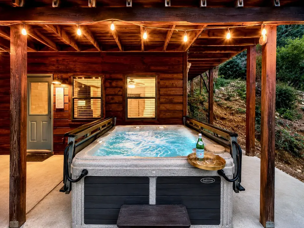 Outdoor hot tub on the cabin's covered lower patio under string lights