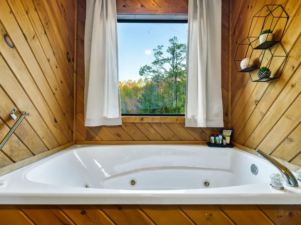 Indoor jacuzzi tub with wood-paneled walls and a window, across from a main-floor king bedroom in the cabin