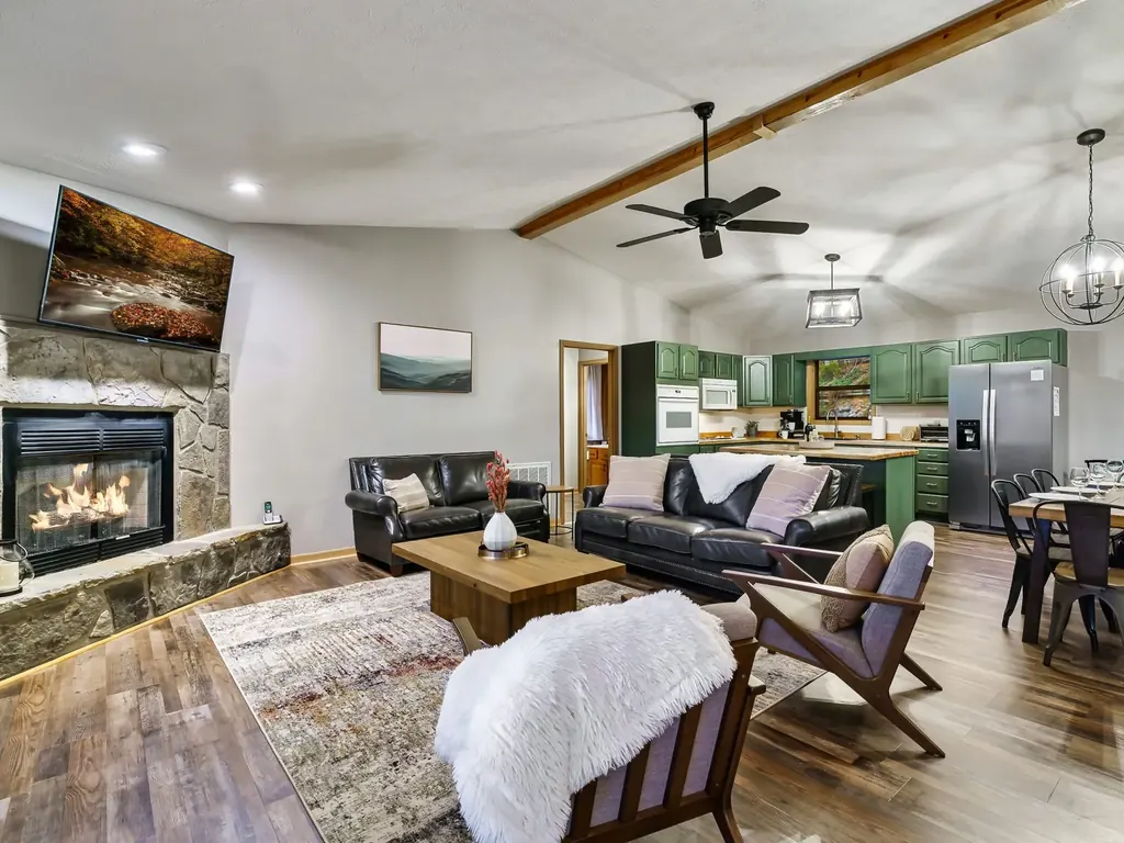 Upstairs living room in the cabin with a stone fireplace, TV and sofas, open to the kitchen