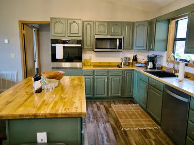 Cabin kitchen with a butcher-block island, sage green cabinets and appliances