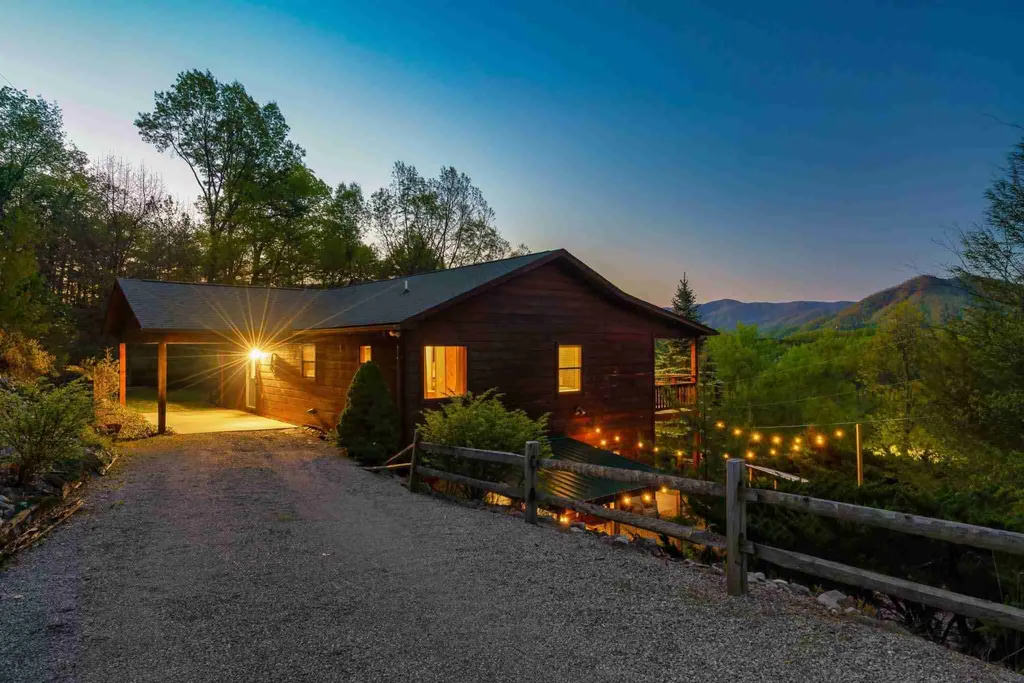 The cabin at twilight with its lights on and mountains behind