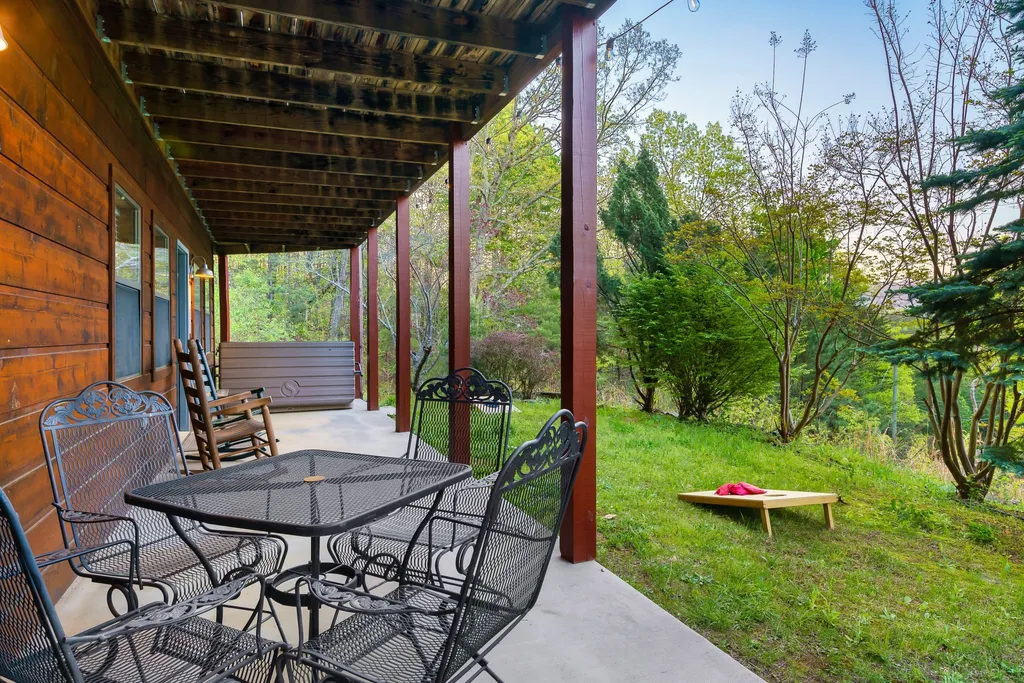Chairs on the cabin's covered lower patio, with a cornhole board on the lawn