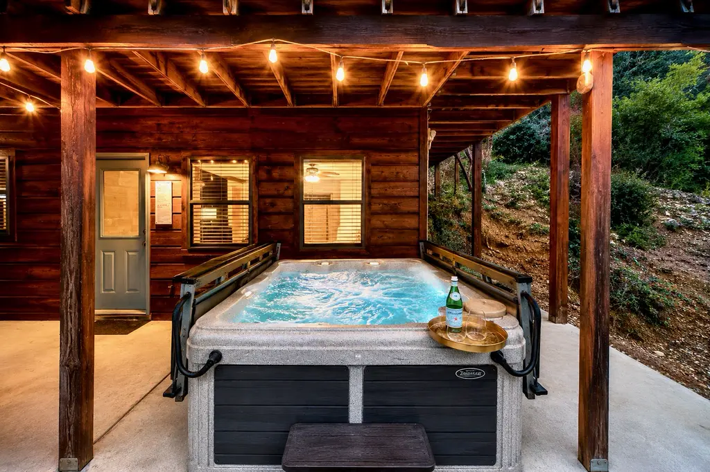 The cabin's hot tub on the covered lower patio, lit by string lights at dusk