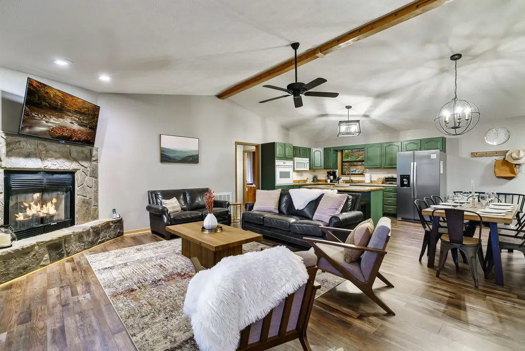 The cabin's open living room with a stone fireplace, leather sofas, dining table and green kitchen