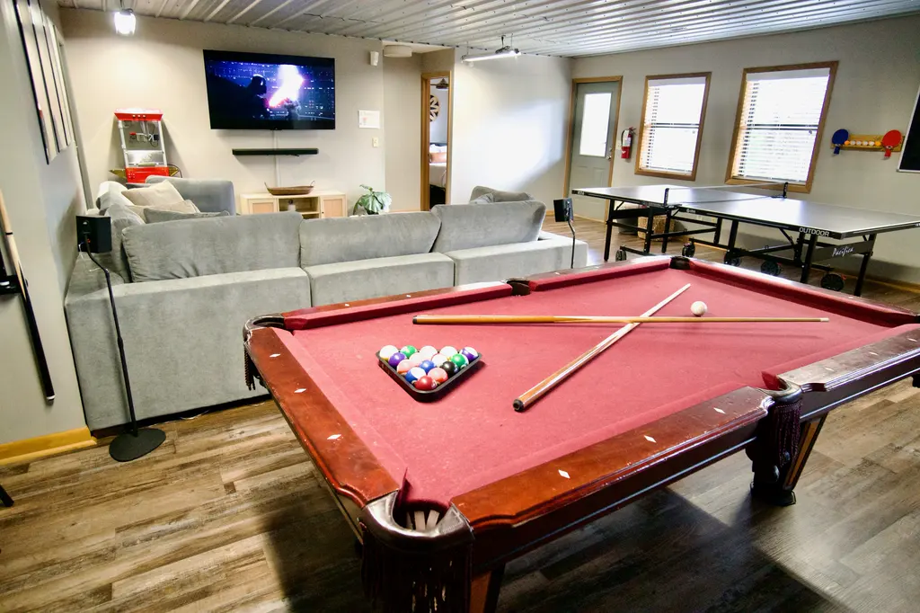 The cabin's game room with a pool table, ping pong table, sectional sofa and TV
