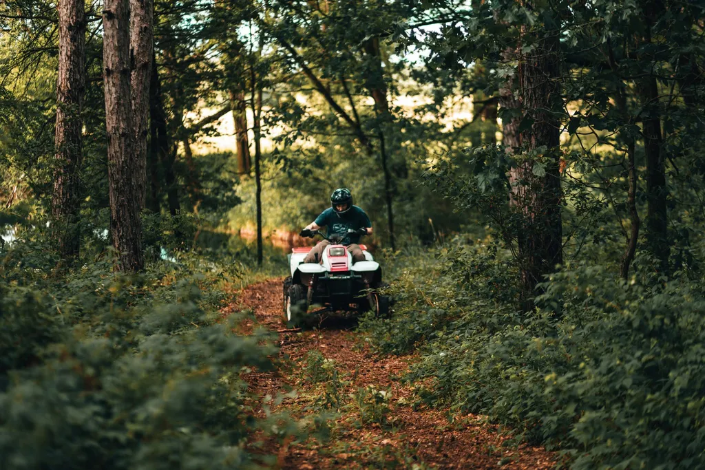 A rider on an ATV coming down a wooded dirt trail