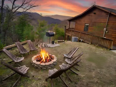 Fire pit lit at sunset with chairs gathered around it beside the cabin