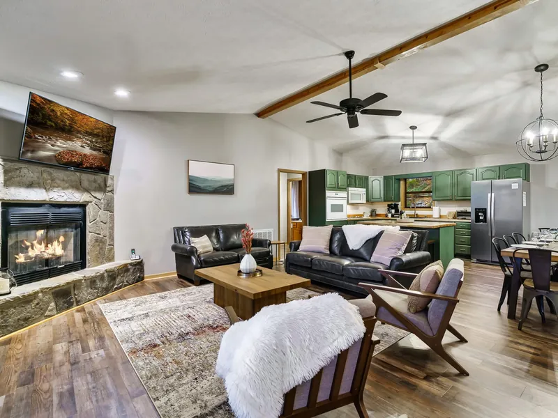Upstairs living room in the cabin with a stone fireplace, TV and sofas, open to the kitchen