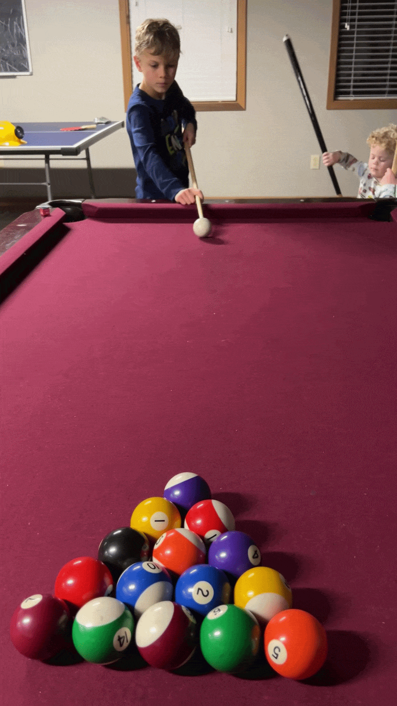Kid shoots cue ball on pool table